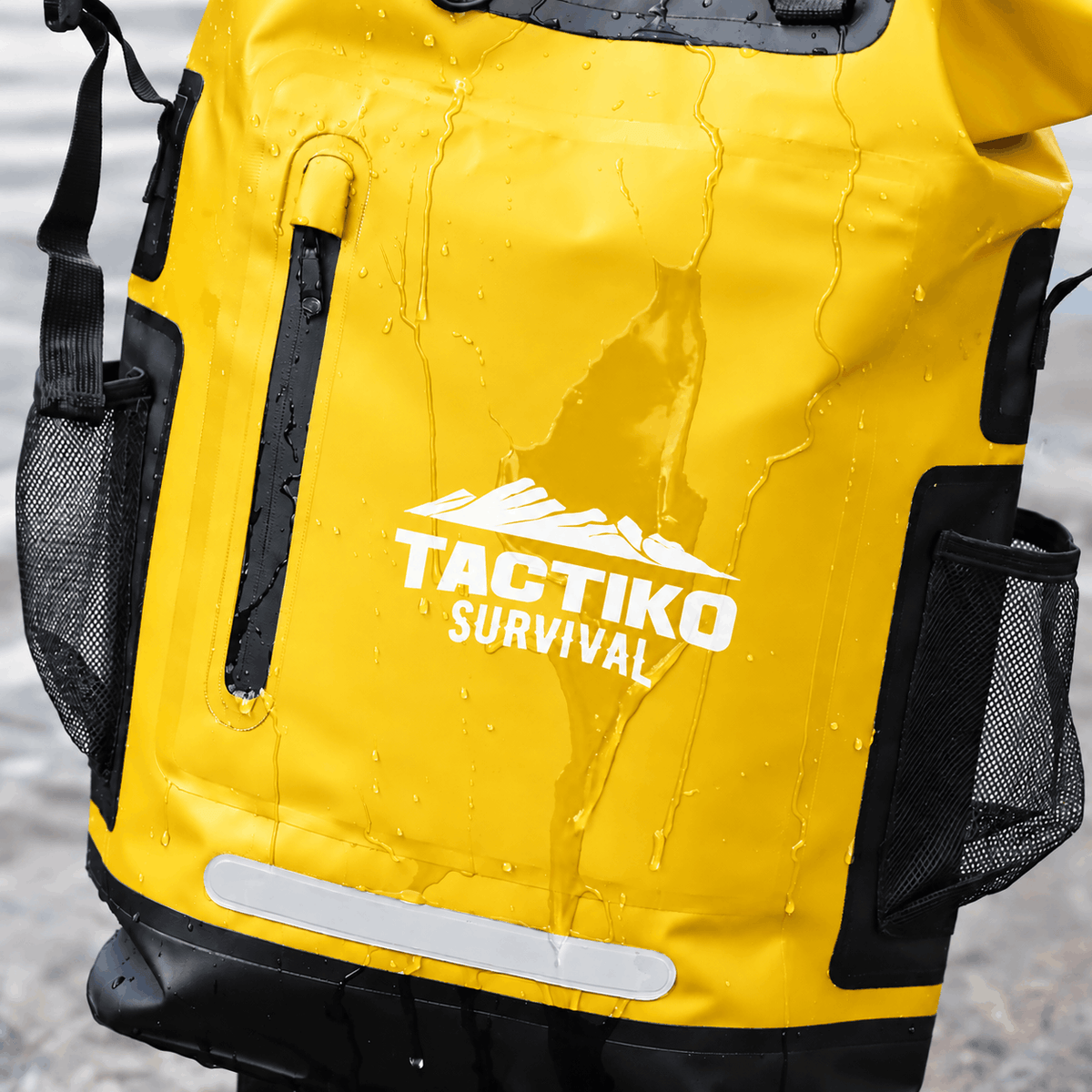A close-up of a bright yellow waterproof backpack with black mesh side pockets and black trim, covered in water droplets. The front features a white printed logo that reads 'TACTIKO SURVIVAL' with a mountain graphic above it.